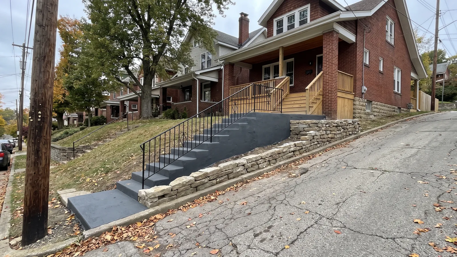 Newly poured concrete front steps and stoop with a black iron handrail leading to the porch of a brick house on a hillside